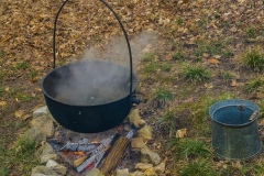 A pioneer's black metal pot hanging over a wood fire cooking sap down into syrup.