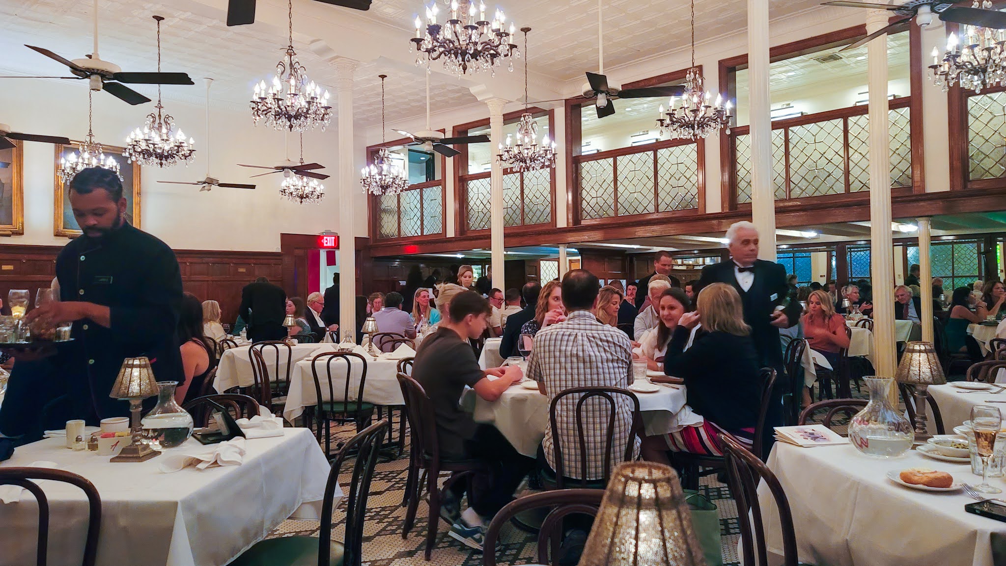 The dining room of Arnaud's restaurant in the French Quarter of New Orleans. Several tables are filled with diners as waiters in black tie work the room.