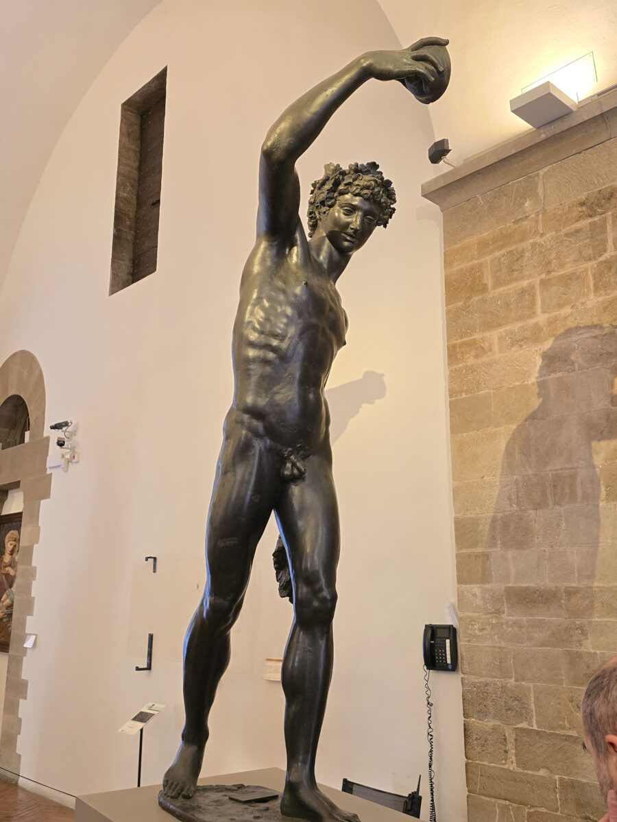 A nude bronze statue of the Roman God of Wine, Bacchus holding a cup of wine above his head