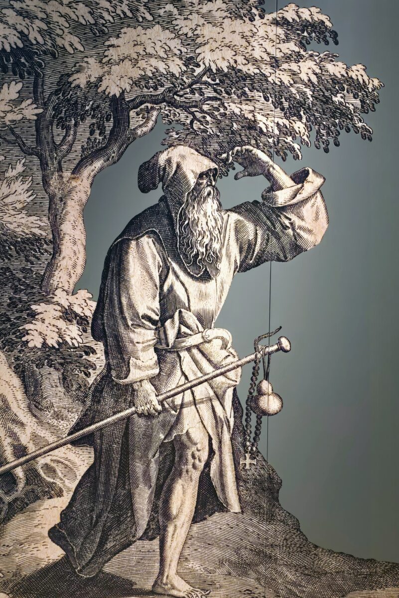 A bearded man in a cloak, carrying a walking stick, gourd for wine, and a crucifix. He is looking off into the far distance. It is a drawing.